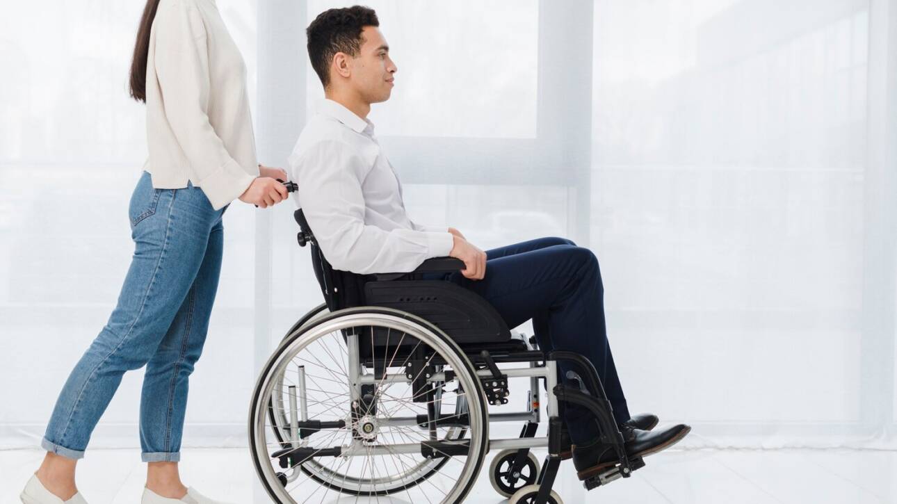 smiling-woman-pushing-young-man-sitting-wheelchair_23-2148127390